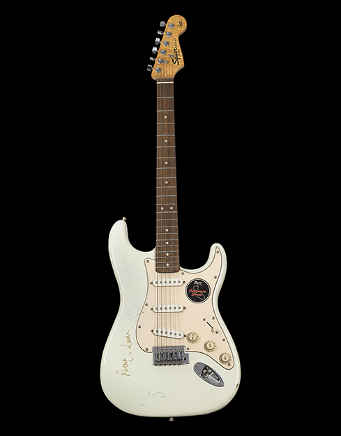 A bright white guitar with prominent circular tone and volume regulators. The base of the guitar has a sticker of Squier Fender, California Series.