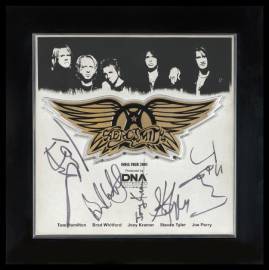 Golden wings at the center with black and white digitally altered faces of Aerosmith band members blending above. Scattered autographs over text DNA India.